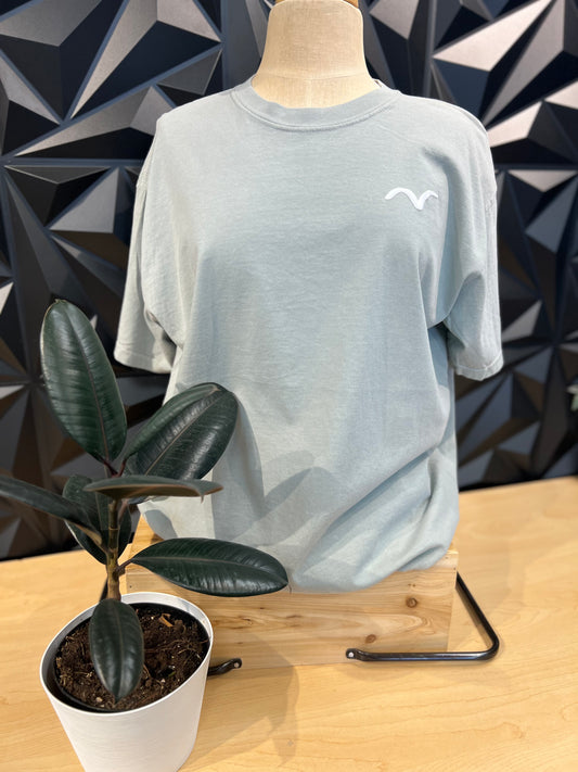 manequin wearing grey set free tshirt on a shelf with black background with white bird symbol on the front left chest