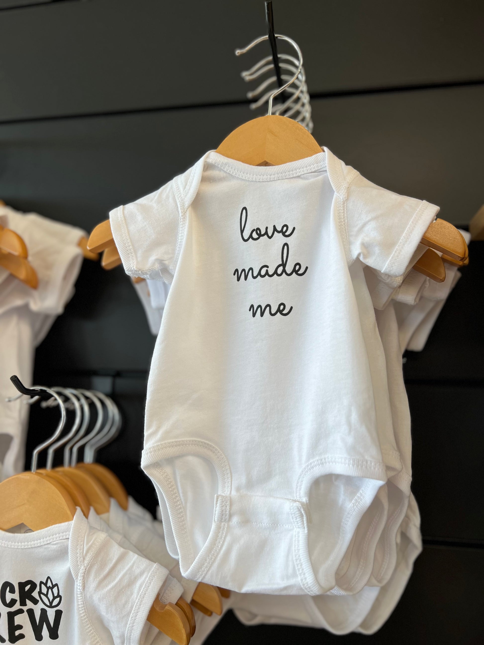 white baby onsie on wood hanger with black letters saying love made me