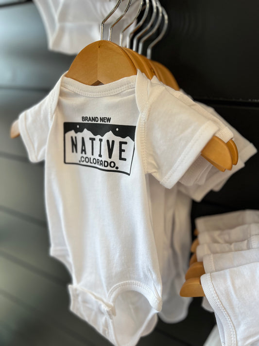 white baby onsie on a wood hanger that says Brand New Native Colorado