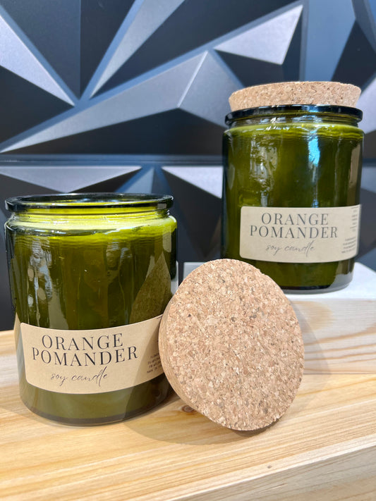 two green glass jar candles with cork lids, tan labels read "Orange Pomander soy candle"