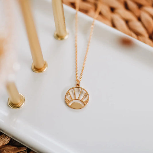 white tray with 3 gold poles sticking up, dainty gold chain with round pendant cut out like a sunrise