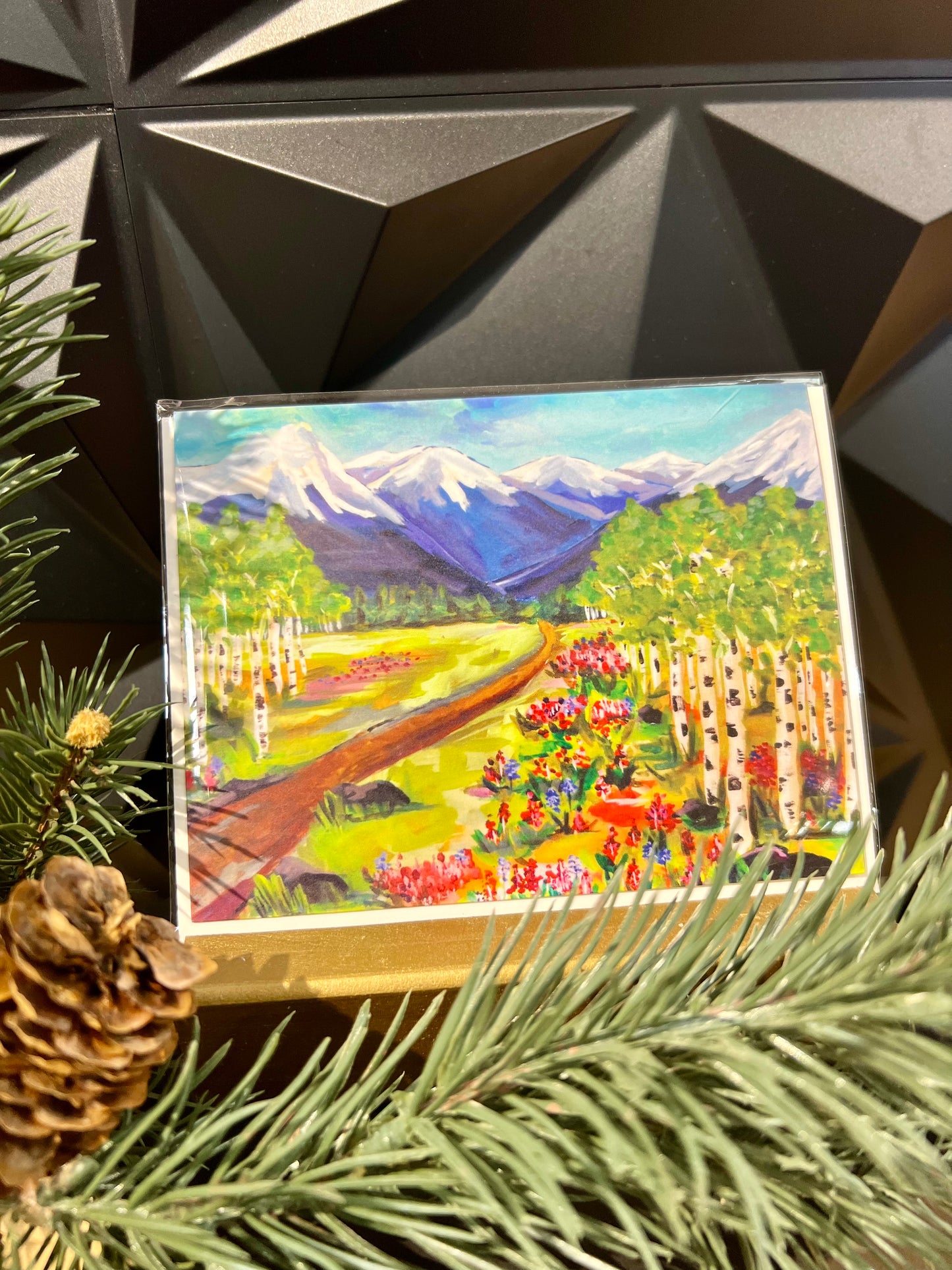rocky mountain landsacape greeting card next to a pine branch on table
