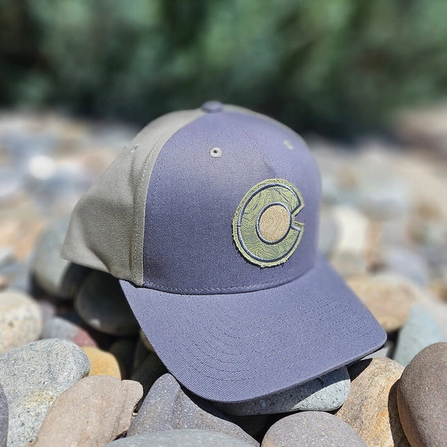 charcoal and olive Colorado C hat laying on rocks in the sun