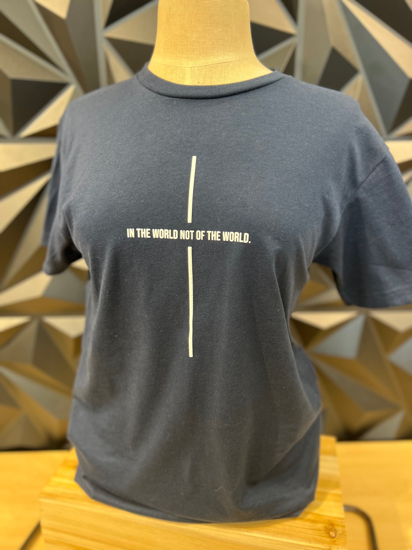 dark blue-grey tshirt with a white line down the middle and words across it to look like a cross - the words say In the world no of the world.