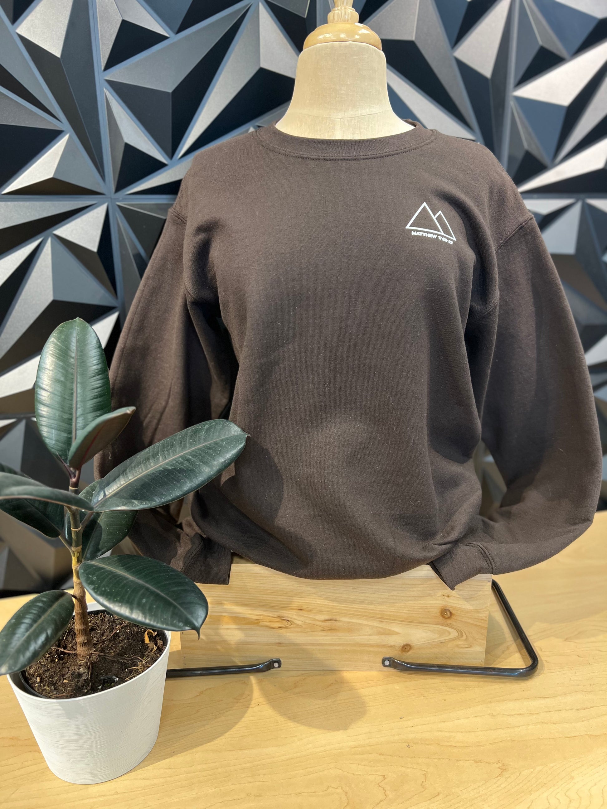 mannequin wearing a dark blue crewneck sweatshirt, showing the front left pocket area has a triangle with mountains peaks words saying HE MOVES MOUNTAINS